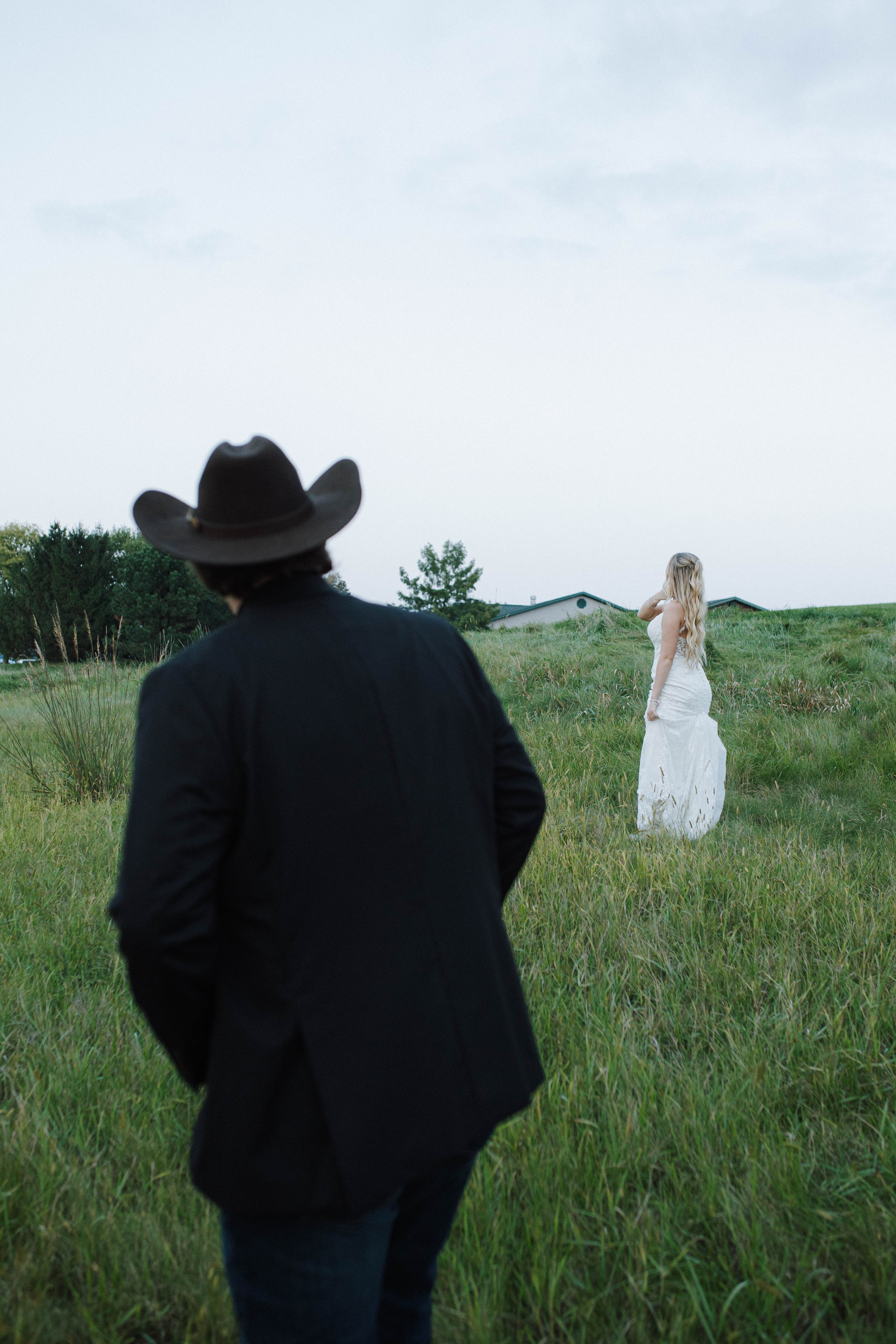Wisconsin wedding photographer - emotional first look moment with groom watching bride in open field with dramatic perspective