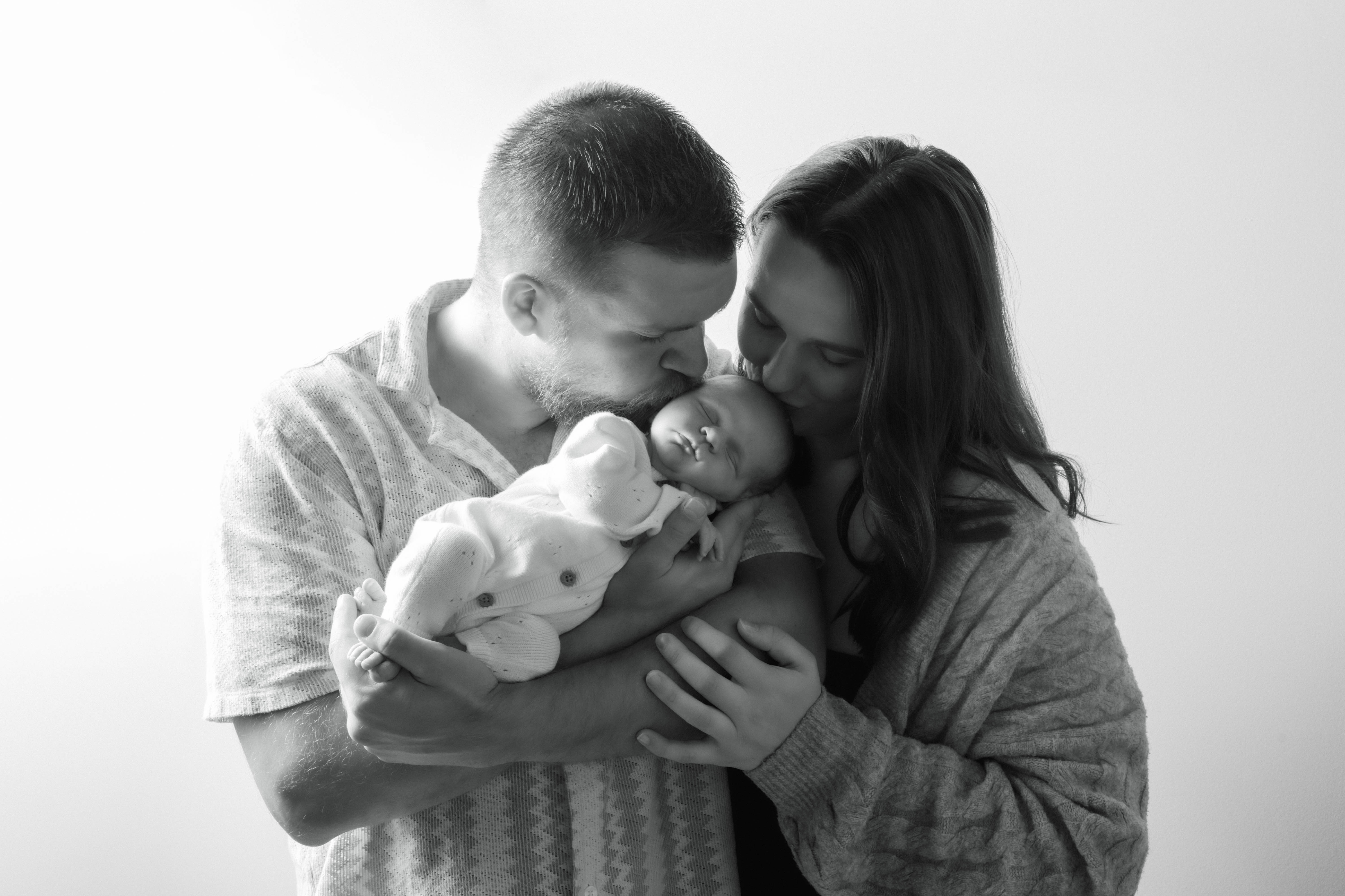 Parents lovingly kissing their newborn baby
